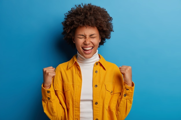 Foto gratuita la donna felice dalla pelle scura gode di un momento di successo, celebra la vittoria o un grande risultato, si sente gioiosa, ottiene obiettivi o risultati importanti