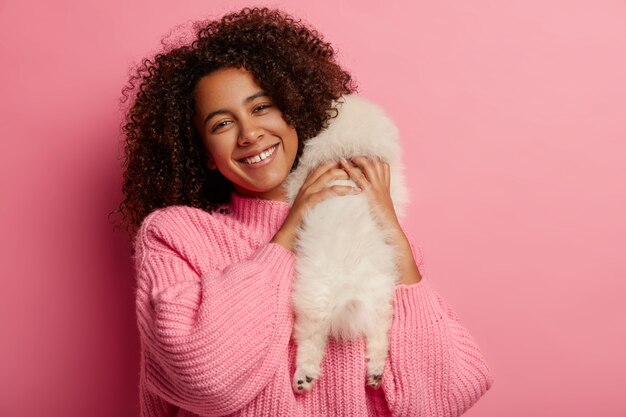 Happy dark skinned woman plays with white spitz dog