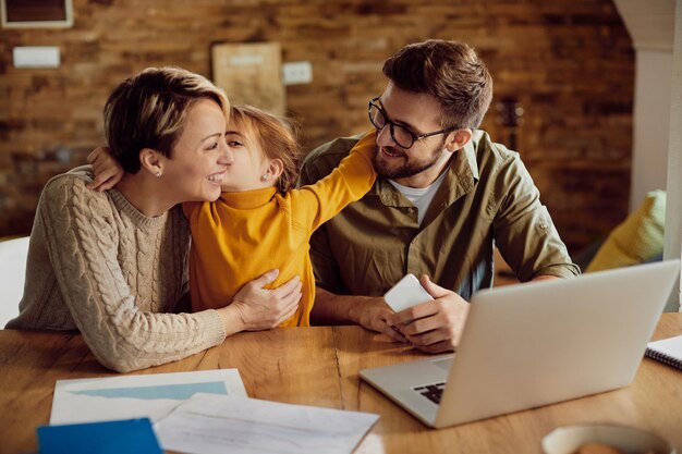 Счастливая дочь обнимает и целует своих работающих родителей дома