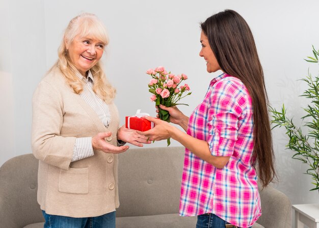 Happy daughter giving wrapped gift box and flower bouquet to her mother