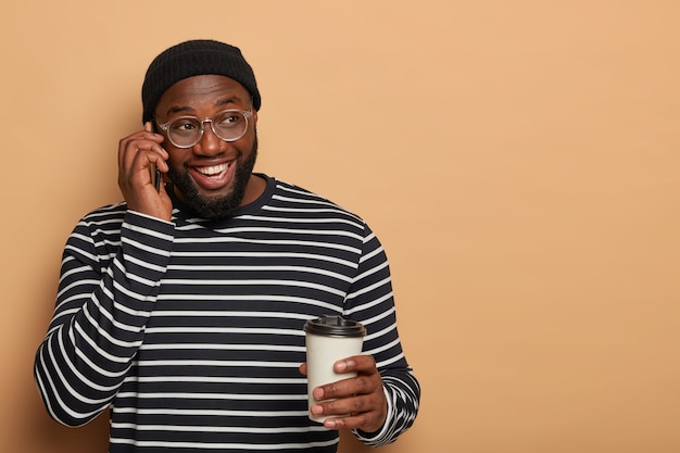 Happy delghted guy with dark skin has cheerful telephone conversation