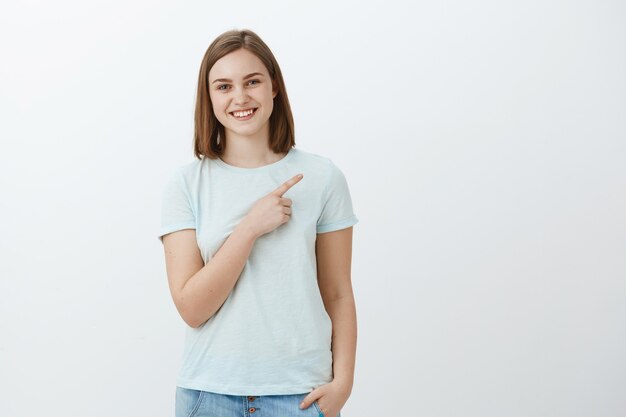 Happy delighted and carefree young woman pointing at copyspace