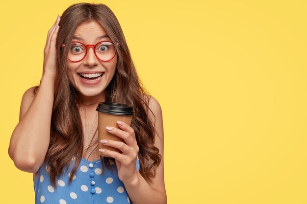 Happy delighted young woman giggles positively, wears round glasses