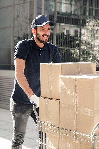 Happy delivery man with cardboard boxes walking on sidewalk