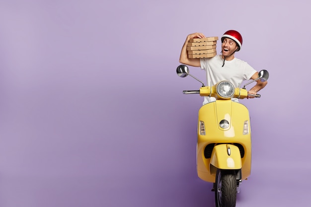 Happy deliveryman driving scooter while holding pizza boxes