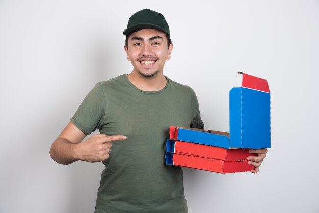 Happy deliveryman pointing at pizza boxes on white background.