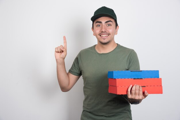 Happy deliveryman pointing at up with pizza boxes on white background.