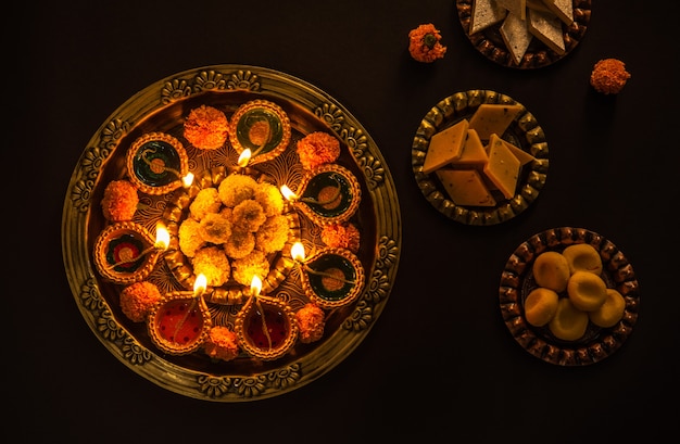 Happy diwali - flower rangoli with sweets or mithai and diya in bowls for diwali or any other festivals in india, selective focus