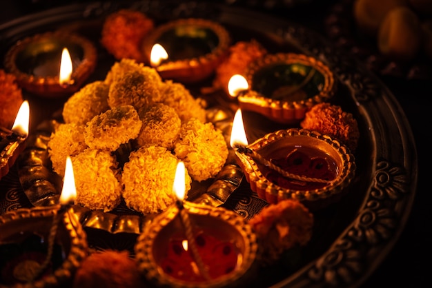 Happy diwali - flower rangoli with sweets or mithai and diya in bowls for diwali or any other festivals in india, selective focus