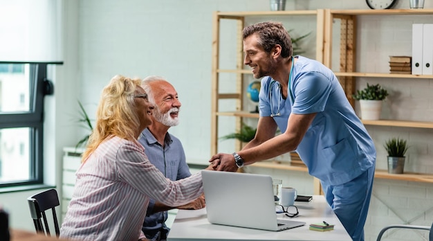 Happy doctor greeting senior couple and shaking hands with a woman at his office