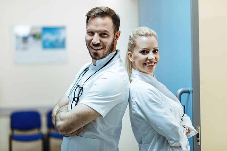 Happy doctor and his female colleague standing back to back with their arms crossed in the hospital and looking at camera