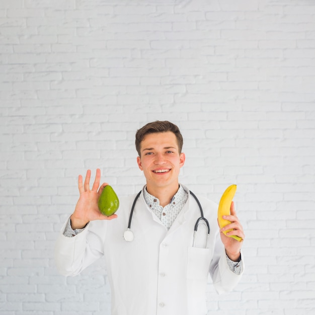 Medico felice che tiene avocado e banana in mani