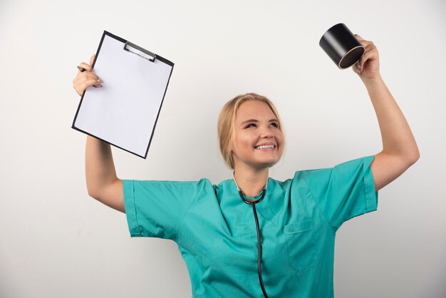 Happy doctor holding clipboard and cup on white.