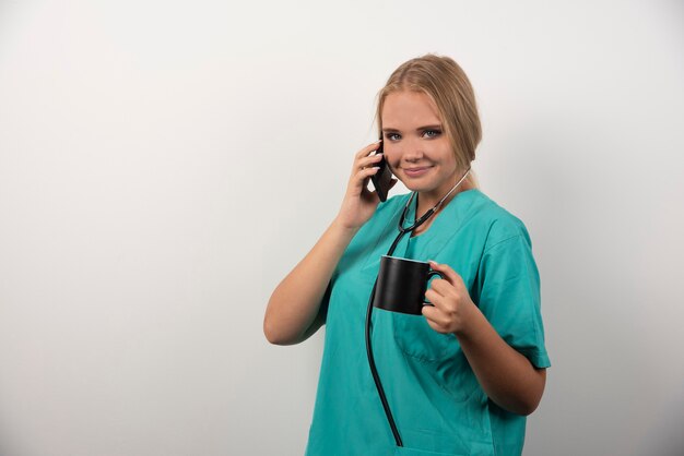 Happy doctor holding tea while talking with telephone.