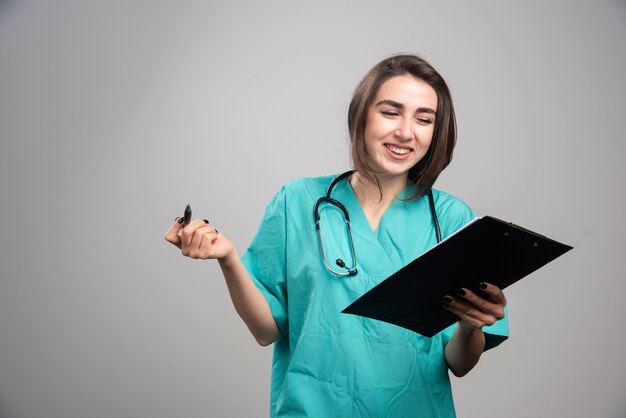 Happy doctor looking at clipboard on gray wall.