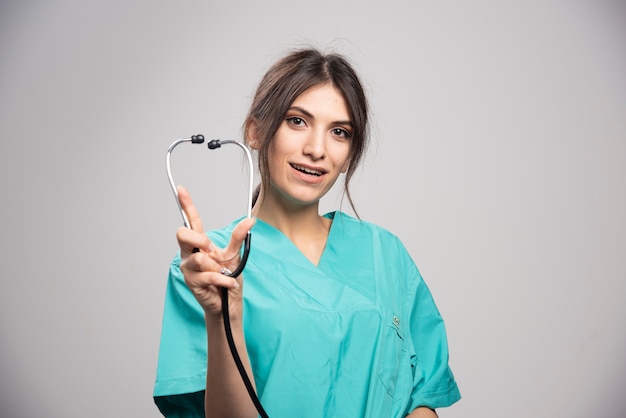 Happy doctor showing stethoscope on gray