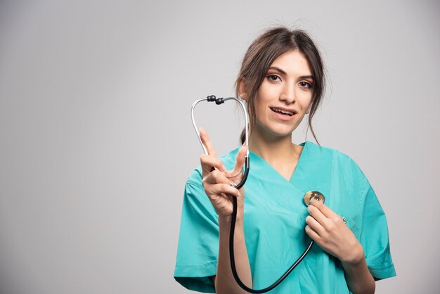 Happy doctor showing stethoscope on gray