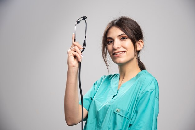 Happy doctor showing stethoscope on gray