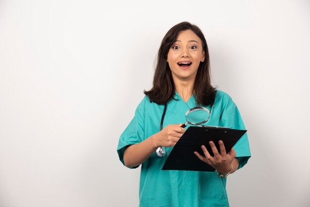 Happy doctor with clipboard and magnifying glass on white background.