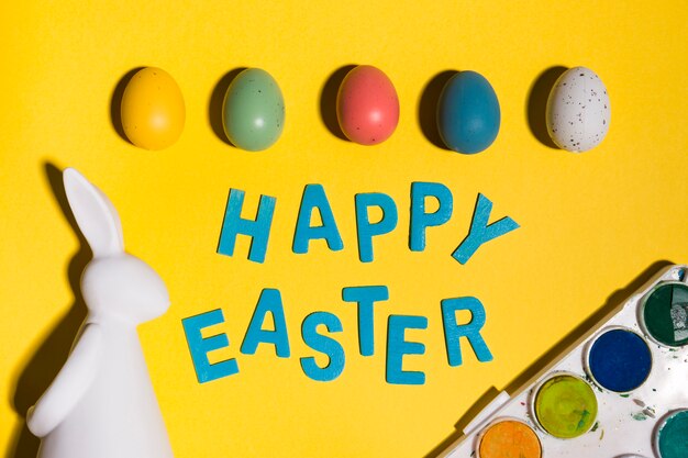 Free photo happy easter inscription with eggs and rabbit on table