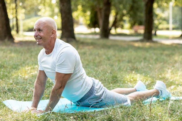 Happy elder man practicing yoga outside