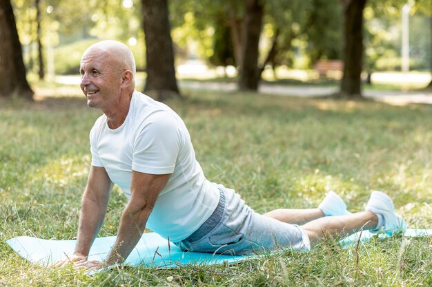 Happy elder man practicing yoga outside