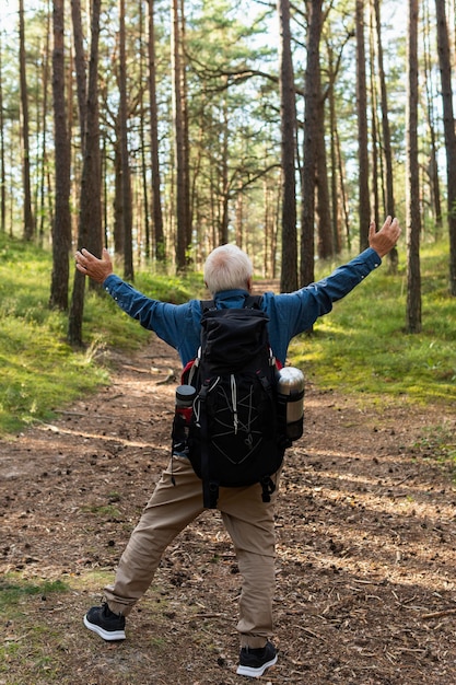 Happy elder man with arms open backpacking in nature