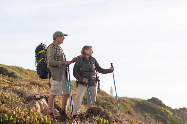 Happy elderly family hiking on summer. Man and woman in casual clothes and with ammunition looking at landscape. Hobby, active lifestyle concept