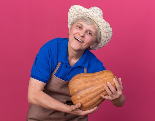 Счастливая пожилая женщина-садовник в садовой шляпе, держащая тыкву