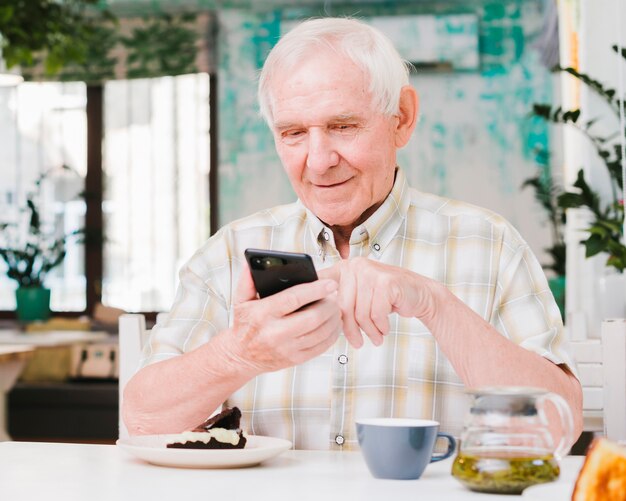 幸せな老人男性のカフェに座っていると携帯電話にテキストメッセージ