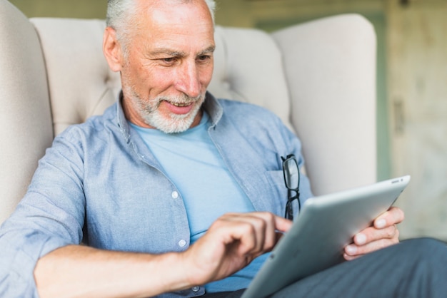 Happy elderly man sitting on armchair using digital tablet