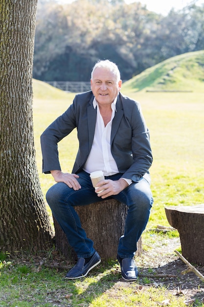 Free photo happy elderly man sitting on a log