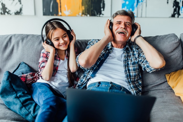 Happy elderly man with a little girl is using a headphones while lying at home.