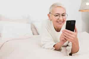 Free photo happy elderly woman in bed holding smartphones