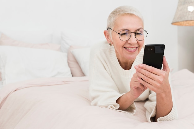 スマートフォンを保持しているベッドで幸せな高齢女性