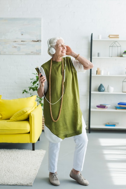 Happy elderly woman enjoying music on headphone at home