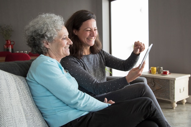 Free photo happy elderly woman and her daughter browsing on tablet computer