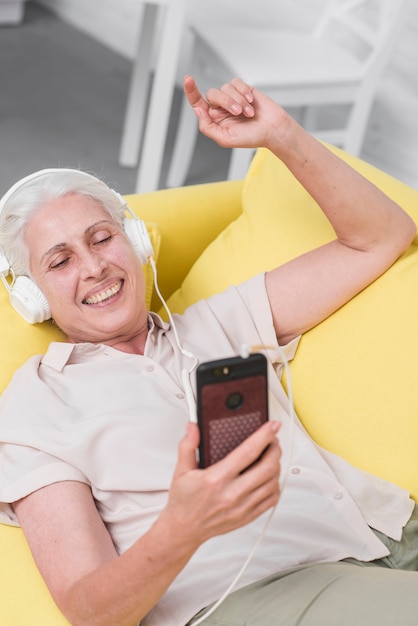 Happy elderly woman listening music on headphone through mobile