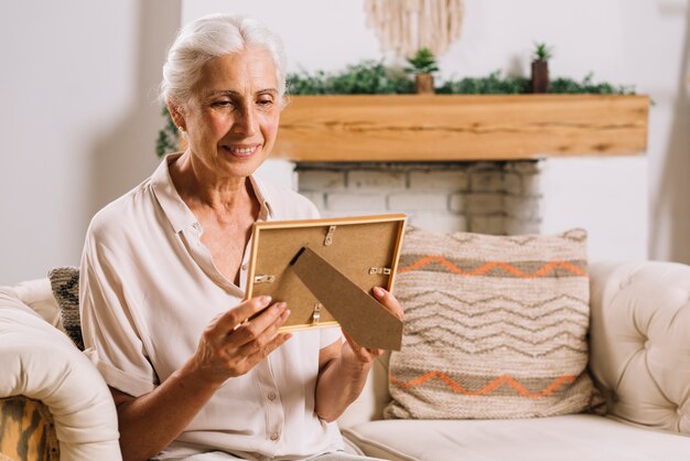Happy elderly woman sitting on sofa looking at photo frame