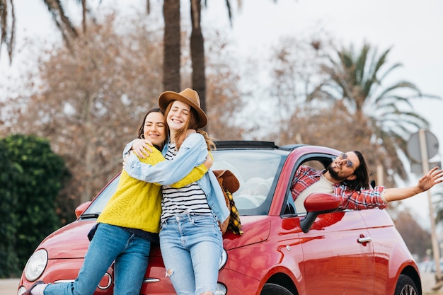 Le donne abbraccianti felici si avvicinano all'uomo che si appoggia fuori dall'automobile