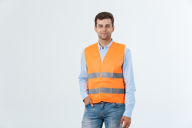笑顔で自信を持って立っている幸せなエンジニア、白い背景で隔離のオレンジ色のベストとカロシャツとジーンズを着ている男。