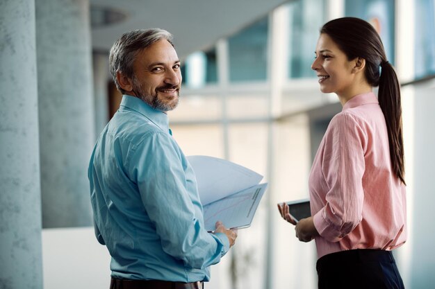 Happy entrepreneur and his female colleague analzying business reports in a hallway