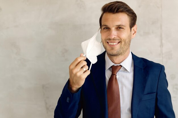 Happy entrepreneur removing protective mask off his face and looking at camera