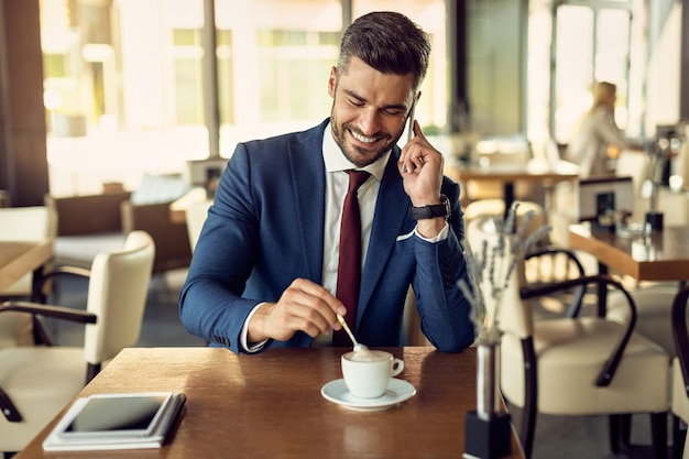 Imprenditore felice che prende il telefono mentre fa una pausa caffè in un bar