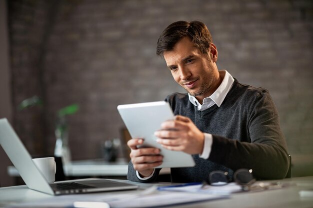 Счастливый предприниматель, использующий цифровой планшет и что-то читающий во время работы в офисе