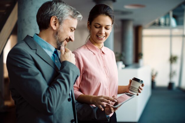 Happy entrepreneurs cooperating while using touchpad in a hallway