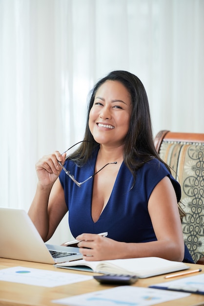 Happy ethnic businesswoman at table in office