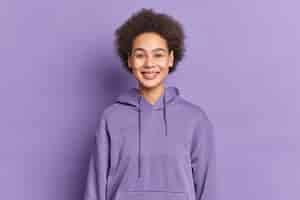 Free photo happy ethnic teenager with afro hair smiles positively wears purple hoodie being in good mood.