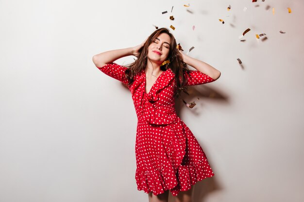 Happy European female model enjoying party and smiling with eyes closed against confetti.