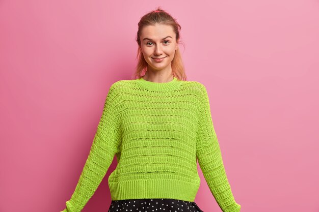 Счастливая европейская девушка в большом вязаном свитере, приятно улыбается, с уверенным выражением лица, искренним взглядом.